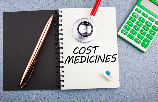 El concepto del costo de los medicamentos. La inscripción COSTO DE LA MEDICINA en un cuaderno junto a medicamentos y un estetoscopio. Costo y costos del tratamiento. photo