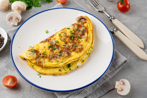 Omelet with fried mushrooms and fresh herbs in a plate on a concrete background. Delicious healthy breakfast. Top view. Copy space