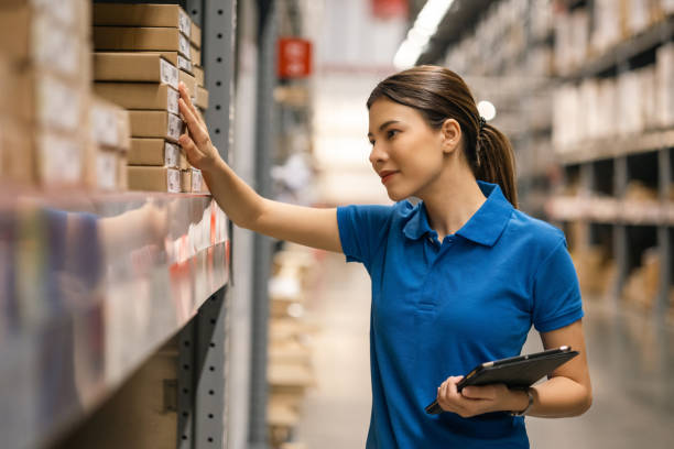 junge arbeiterin in blauer uniform checkliste verwalten paketkastenprodukt im lager. asiatische mitarbeiterin mit tablet, die in der ladenbranche arbeitet. logistisches importexportkonzept. - warehouse worker stock-fotos und bilder