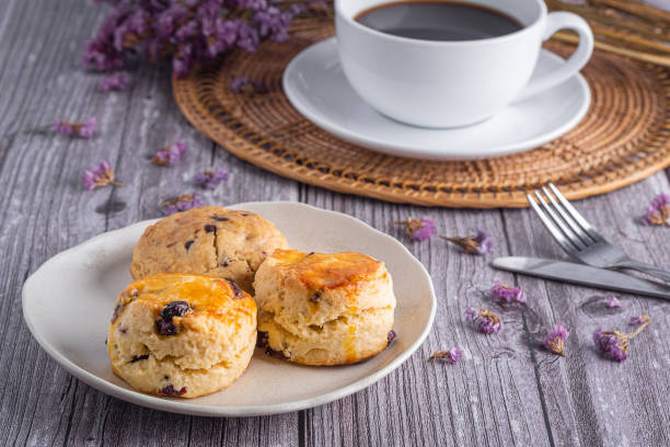 istock Traditional British scones and a cookie on a plate with a white coffee cup on a wooden table with a flower blurred background 1430582720