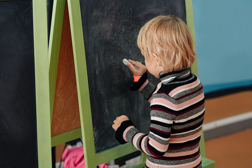 Child drawing with white chalk on a blackboard.