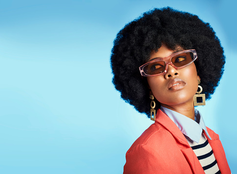 Fashion, color and african woman in studio with copy space posing or by blue background. Young, beautiful and black model with natural afro and trendy, edgy and hipster clothes with funky sunglasses.