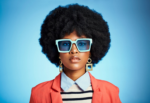 Fashion, beauty and makeup with black woman and sunglasses against a blue background in studio for luxury, model and designer. Cosmetics, creative and color with portrait of girl with afro hairstyle