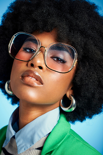 Fashion, makeup and beauty with black woman and sunglasses against a blue background studio. Cosmetics, afro hair style and creative portrait of young girl for luxury, lifestyle and designer clothing