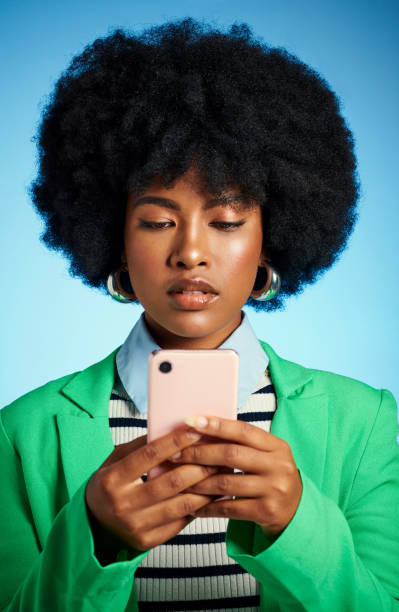 femme noire avec téléphone lisant les médias sociaux, les nouvelles ou les publications en ligne et message texte à contacter contre l’arrière-plan bleu de la maquette du studio. modèle afro sur internet avec une application mobile smartphone avec  - android phone photos et images de collection