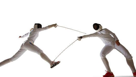 Front view. One sportsman, female fencer in white fencing costume in action, motion isolated on white background. Sport, youth, hobbies, achievements, goal. Girl practicing with rapier