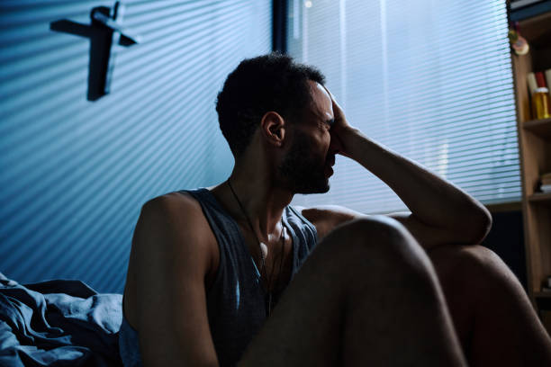 istock Young stressed man touching head while sitting by bed after sleepless night 1430592817