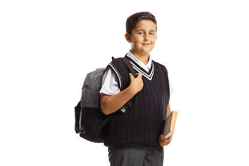 Schoolboy in a uniform holding a book and carrying a backpack isolated on white background