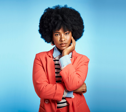 Stylish, fashion and serious black woman with a natural afro and beautiful face while standing against a blue studio background. Portrait of an African female feeling confident in a smart casual suit