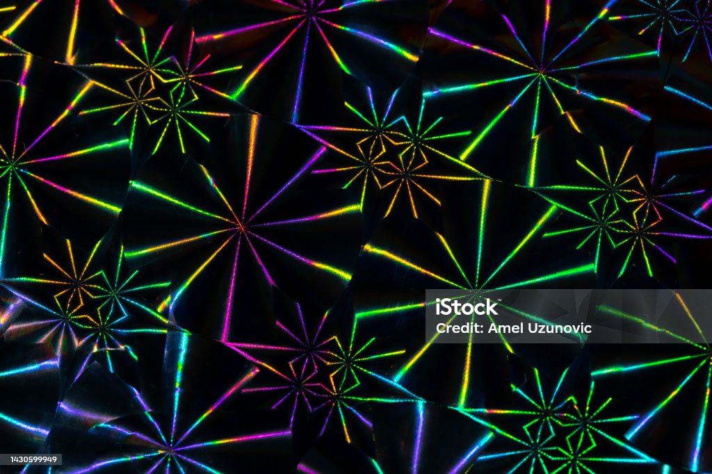 Close up photo. Vibrant holographic neon colors repeating geometric decorative pattern on a reflecting shiny surface hit by light. 90s disco party background. 1990-1999 Stock Photo