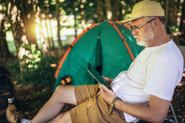 istock Mature man sitting in front of a tent and using digital tablet 1430600201