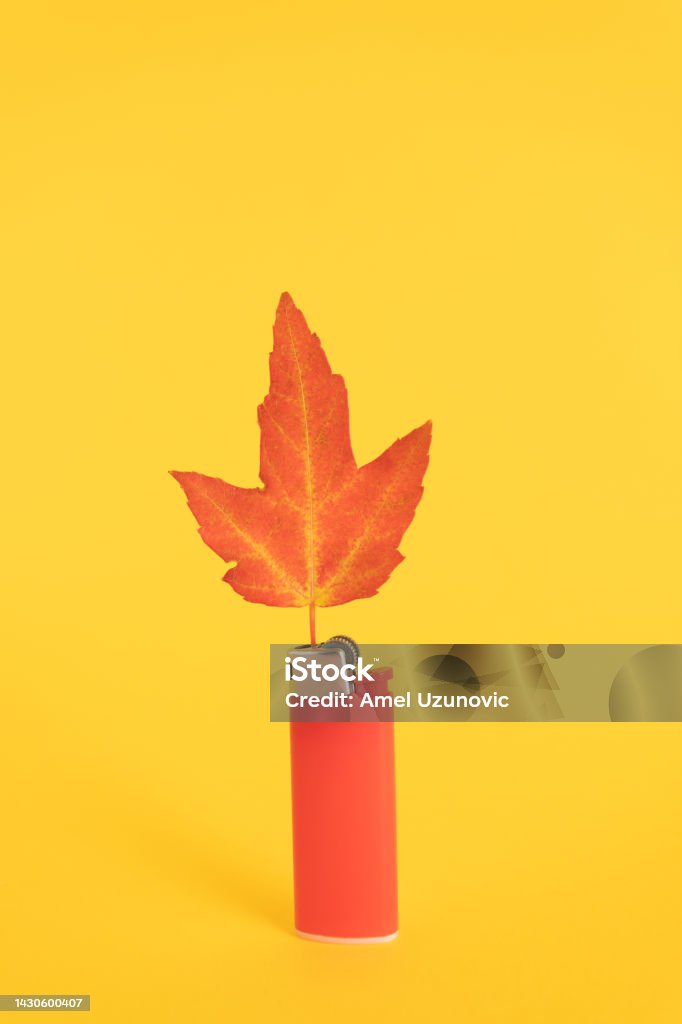 A red lighter and a maple leaf on a yellow background. Autumn colors creative minimal concept. Abstract Stock Photo