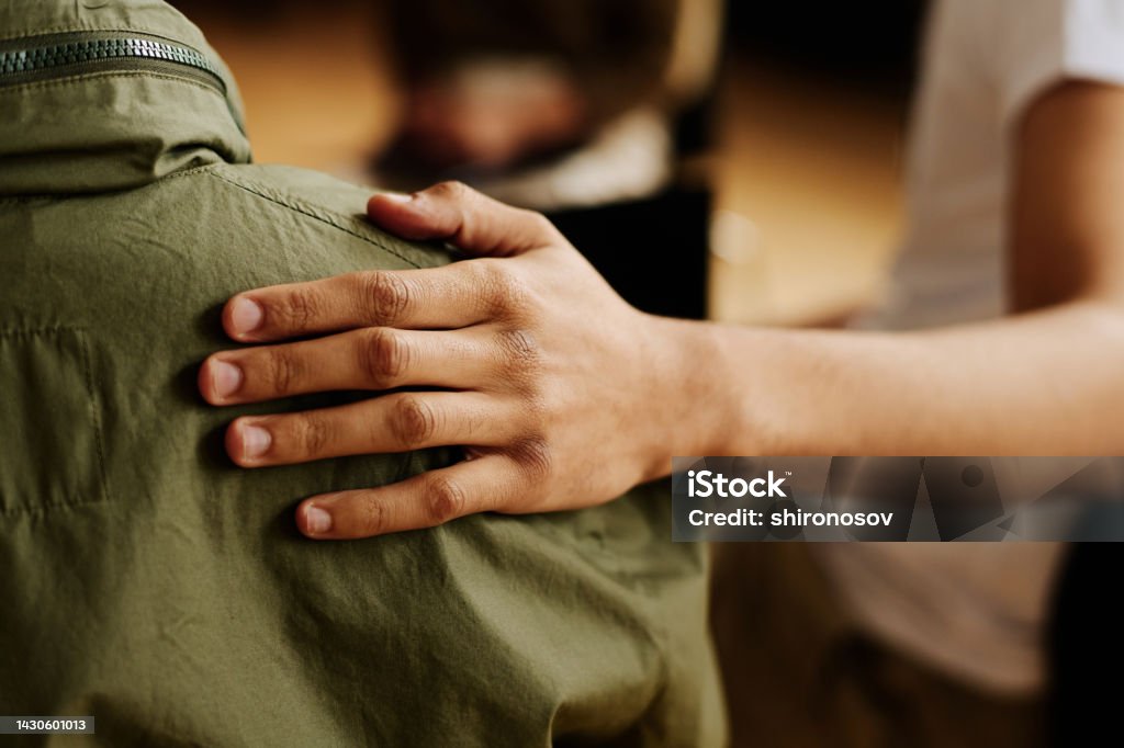 Hand of young supportive man consoling his friend with post traumatic syndrome Hand of young supportive man consoling his friend or one of attendants with post traumatic syndrome caused by dramatic life event Support Stock Photo