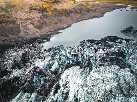 Sólheimajökull is an outlet glacier of the mighty icecap of Mýrdalsjökull on the South Coast of Iceland. The glacier is melting rapidly owing to warmer annual temperatures due to climate change. Aerial drone view of a river created by the melting glacier.