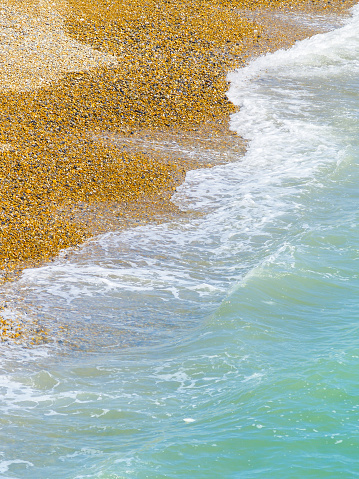 Waterline on Brighton Beach close-up sea washing in on orange coloured pebbles in vertical composition.