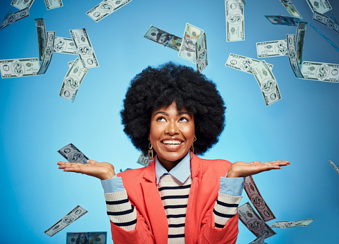 Success, rain and cash with black woman and money against a blue background in studio for finance, investment or dollar. Wow, motivation and financial with happy girl and deal, winner or sale