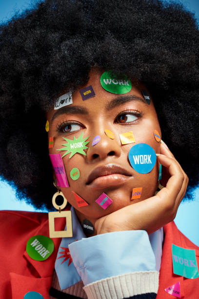 Overworked black woman with work stickers on face, an afro and looking serious. Creative, artistic portrait of bored employee near burnout and mental health related issues like stress or depression mujer negra sobrecargada de trabajo con pegatinas de trabajo en la cara, afro y con aspecto serio. retrato creativo y artístico de un empleado aburrido cerca del agotamiento y los problemas relacionados con la salud mental, como el estrés o la depresión