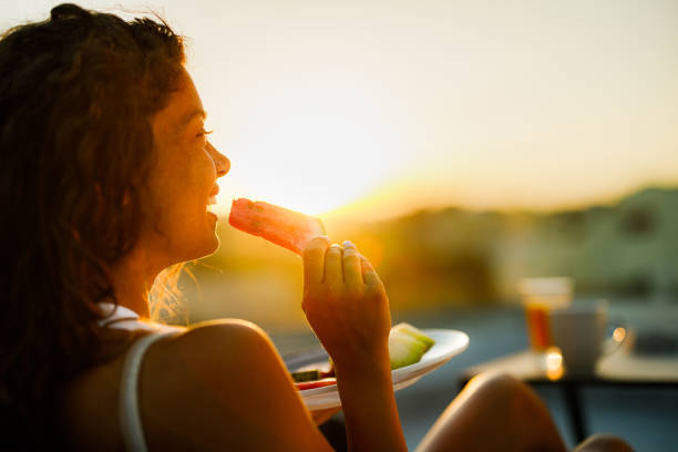 Happy woman enjoying while eating fresh fruit on a terrace at sunset.