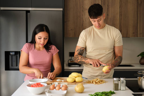 istock Two young latin people peeling potatoes and cutting onion at kitchen. 1430617786