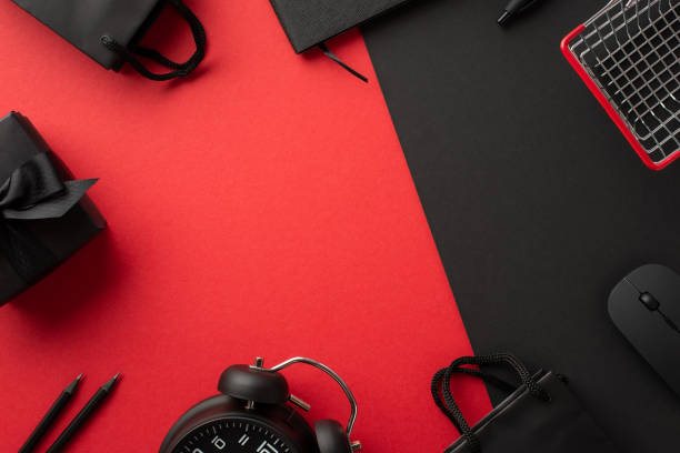 Black friday concept. Top view photo of computer mouse giftbox with bow shopping cart alarm clock paper bags notebook and pencils on bicolor red and black background with copyspace in the middle concepto black friday. vista superior foto de la caja de regalo del ratón de la computadora con arco carrito de compras reloj despertador bolsas de papel cuaderno y lápices sobre fondo rojo y negro bicolor con espacio de copia en el medio