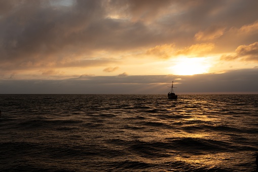 Ship silhouette at sea in the distance during sunset with colorful orange clouds and waves