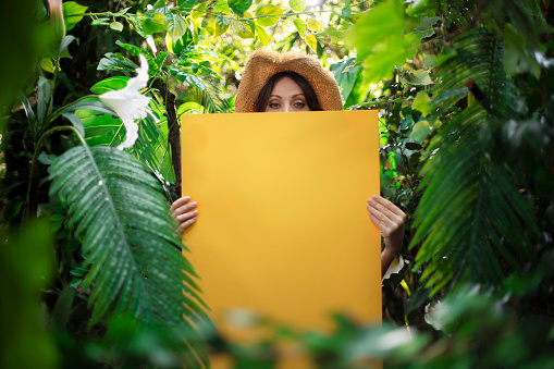Woman showing empty yellow banner among an exotic jungle