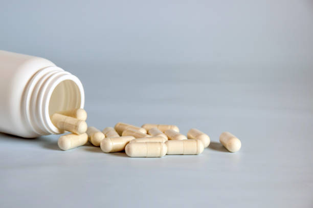 istock Natural yellow pressed medicinal herb,pills in open upturned plastic jar on table front. Alternative medicine concept of drugs, tablets, medicines and pills on gray background. Copy space. 1430620754