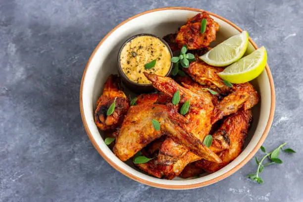 Chicken Wings in a Bowl with Lemon and Sauce Garnished with Fresh Herb Top Down Photo