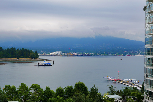 Vancouver waterfront view of the bay, landscape with mountains, waterplane, lake, platform and building. Rainy and cloudy atmosphere.