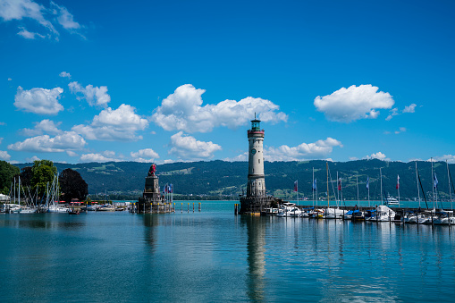 Germany, Lindau island city harbor lighthouse and boats anchoring in beautiful mountain panorama in water of bodensee lake on sunny day