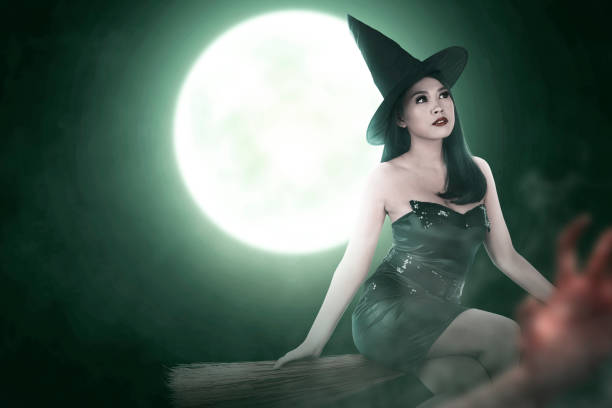 Little growling witch in fancy dress and hat standing in darkness in front of camera and frightening you on Halloween night