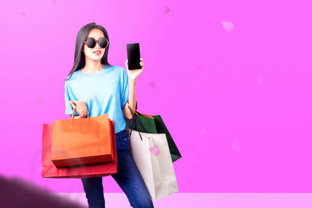 istock Asian woman with sunglasses showing a mobile phone with an empty screen while carrying a shopping bag 1430630835