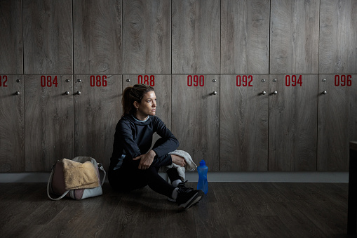 Tired female athlete having a break at gym's locker room. Copy space.