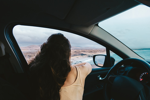 Woman looking at beautiful landscape from her car - road trip concept