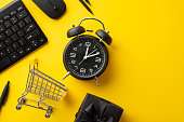 Cyber monday concept. Top view photo of alarm clock keyboard computer mouse shopping cart pencils and giftbox with ribbon bow on isolated yellow background