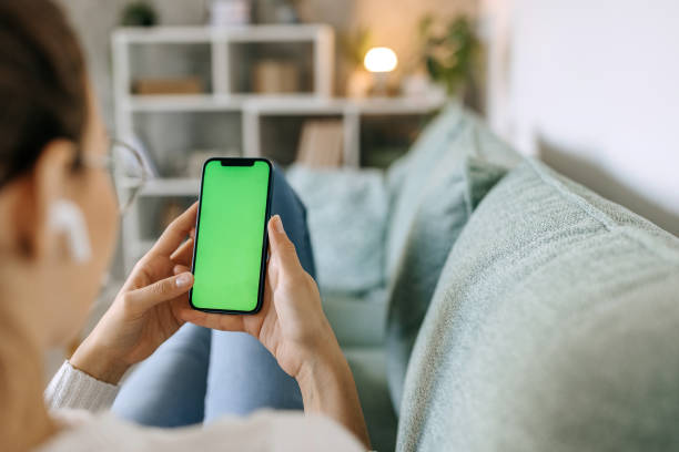 Young woman using phone with green screen while relaxing on the sofa