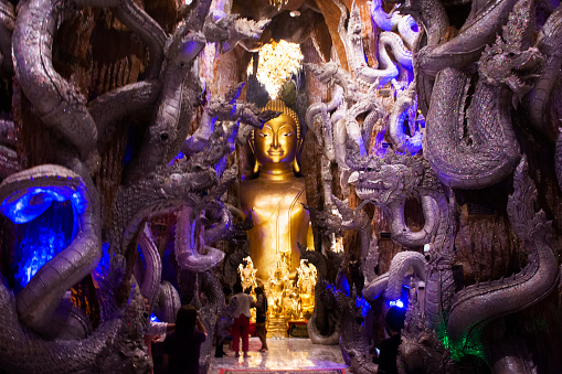 Golden buddha image statue and naga guardian of Wat Maniwong for thai people travel visit tunnel cave and respect praying blessing holy worship mystical at Mani Wong temple in Nakhon Nayok, Thailand