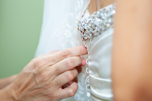 Unrecognizable woman, mother of the bride buttoning up her daughter's wedding dress