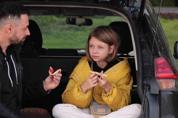 Weekend with family. A little girl came fishing with her parents in the fall and decided to have a bite of pizza in the car a little girl came fishing with her parents in the autumn and sat down to eat pizza in the car in nature, in the open trunk of the car. people family tailgate party outdoors stock pictures, royalty-free photos & images