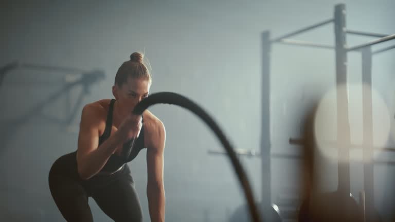 Workout, fitness and battle ropes with a sports woman training with heavy equipment in a gym for exercise. Health, wellness and cardio with a strong female athlete exercising in a sport facility