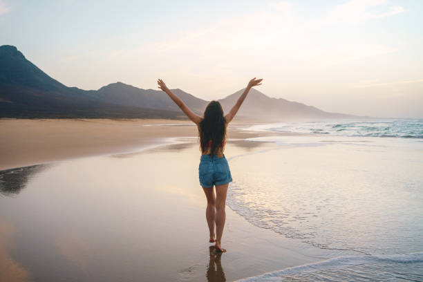 giovane donna felice che cammina da sola sulla spiaggia al tramonto - light sea low tide fuerteventura foto e immagini stock