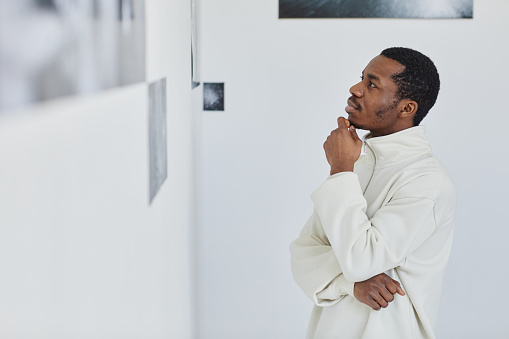 Side view portrait of handsome black man looking at images in photo gallery and enjoying art, copy space