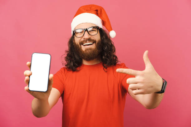 istock Curly bearded man wearing a Christmas cap points at the empty phone screen. 1430669258