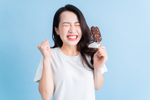 Young Asian woman eating ice cream on background