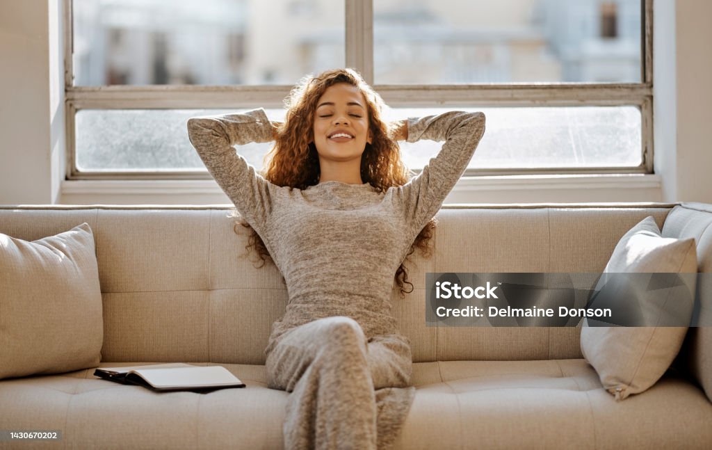 Black woman, relax and resting on living room sofa on holiday vacation or break at home. Calm African female relaxing on couch in South Africa apartment for relaxation and stress relief at the house Relaxation Stock Photo