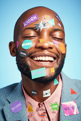 Face, work and sticker with a business man in studio on a blue background with stickers on his head. Happy, motivation and success with a black male employee with a smile and positive attitude