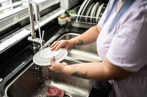 Close-up of mid adult woman washing dishes in the kitchen at home