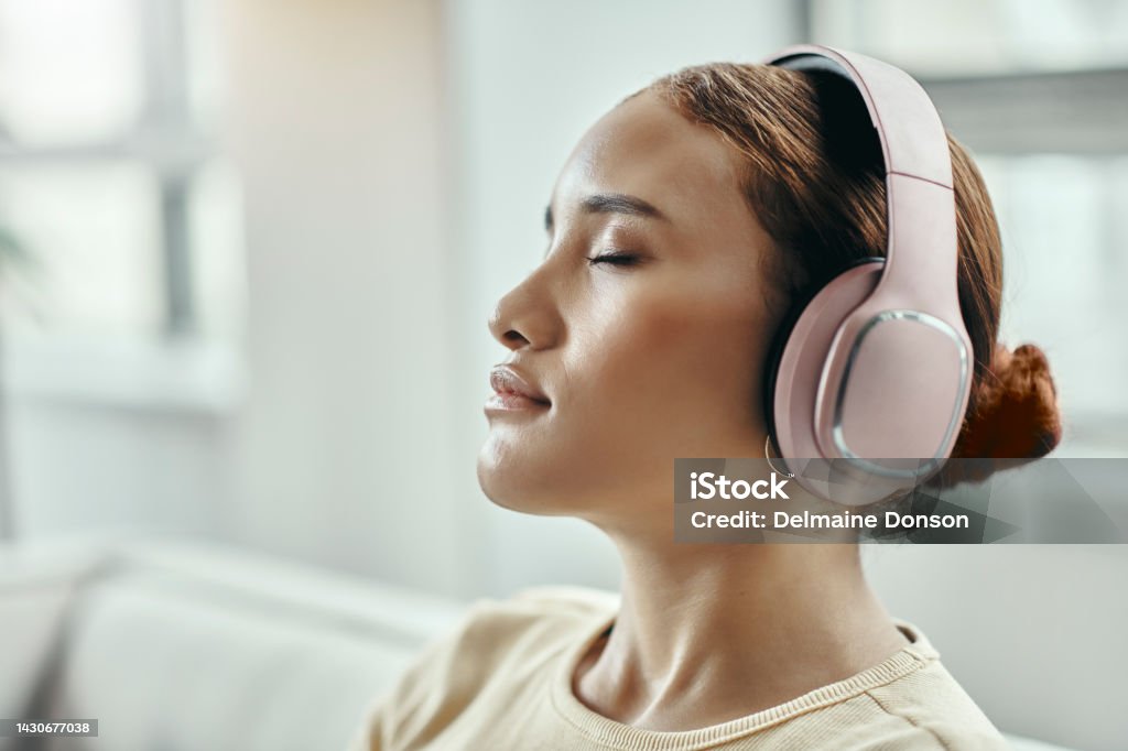Black woman, relax with headphones on sofa and listening to meditation podcast or music in home. Woman on mental wellness break, in her living room and relaxes in peace with no stress or audio Black woman, relax on sofa and listening to music on headphones from home. Woman taking a break, chilling in living room and comfort of house. Eyes closed, no stress and at peace with mental wellness Music Streaming Service Stock Photo
