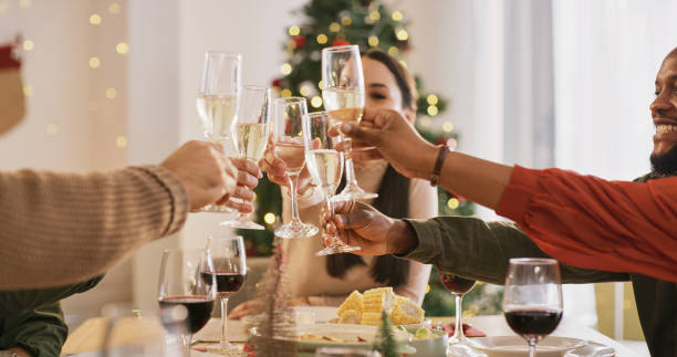 Christmas celebration, champagne toast and friends or group of people at dining room table with food and drink. Celebrate, thanksgiving holiday and family or group of people cheers alcohol wine glass stock photo