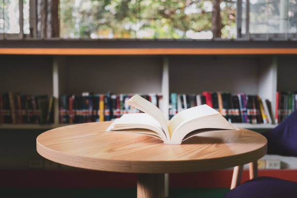 istock An open book or textbook in the library with light from the window on the reading table and the corridor of the bookshelves in the school classroom background.Education learning concept 1430678594